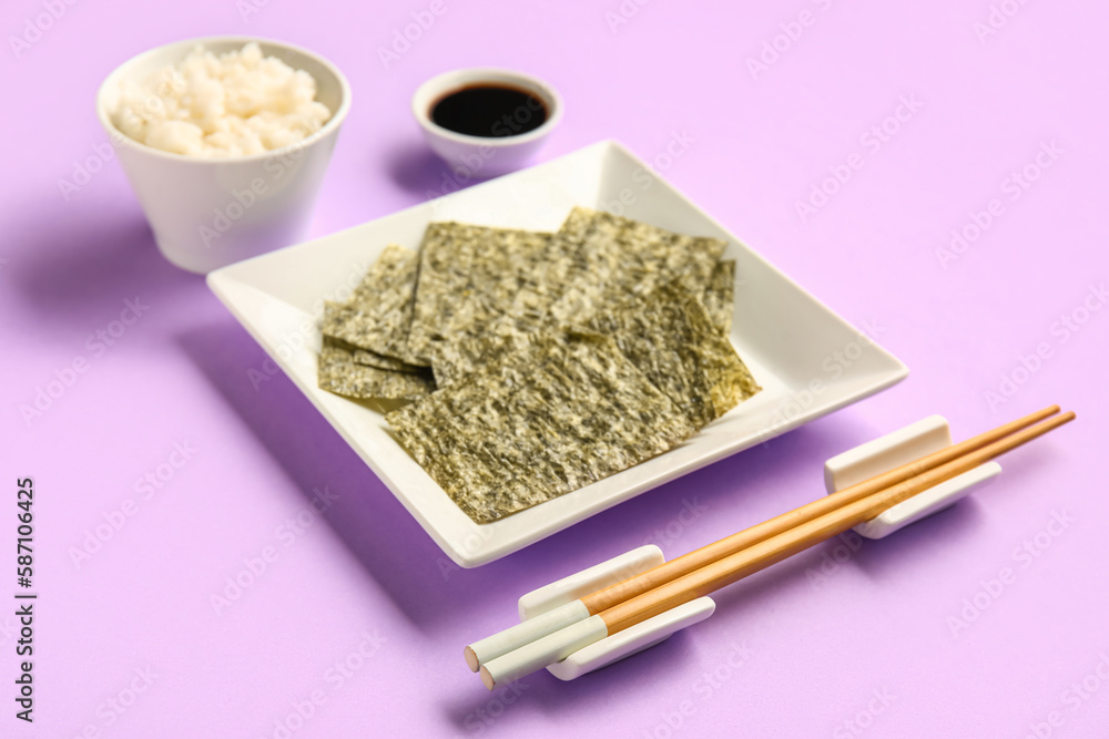 Plate with nori sheets, chopsticks, rice and soy sauce on color background