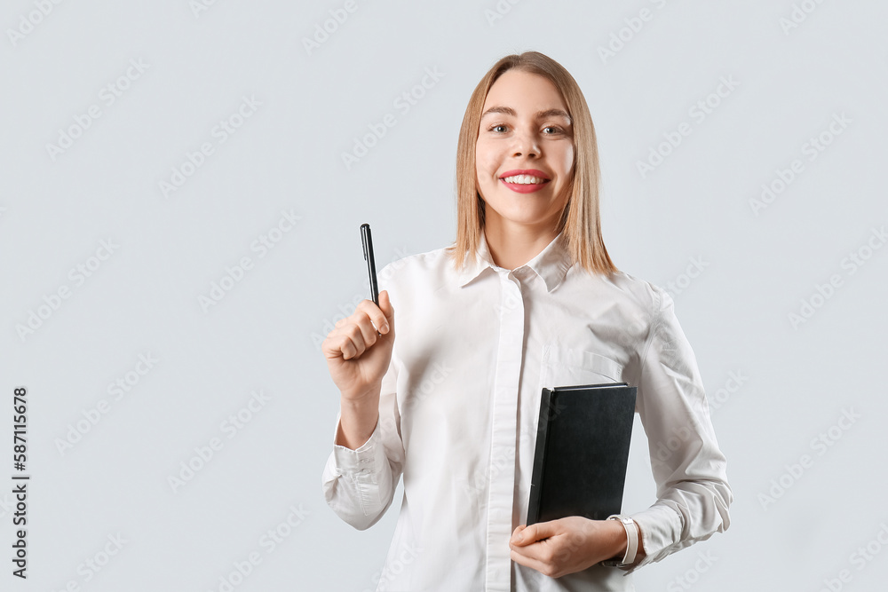 Female business consultant with pen and notebook on grey background