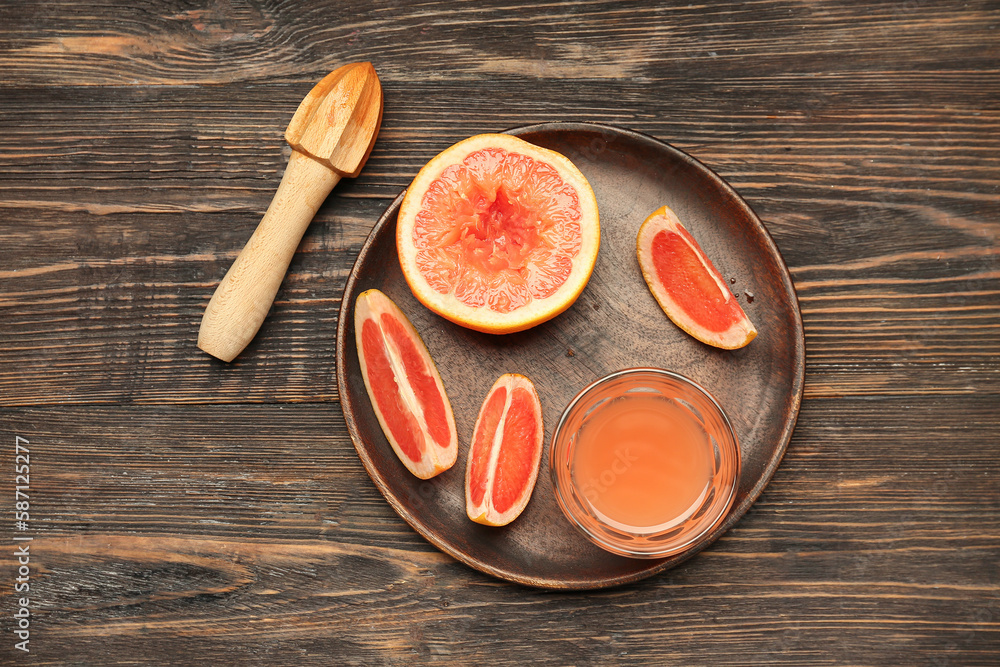 Plate with cut ripe grapefruit and glass of juice on wooden background