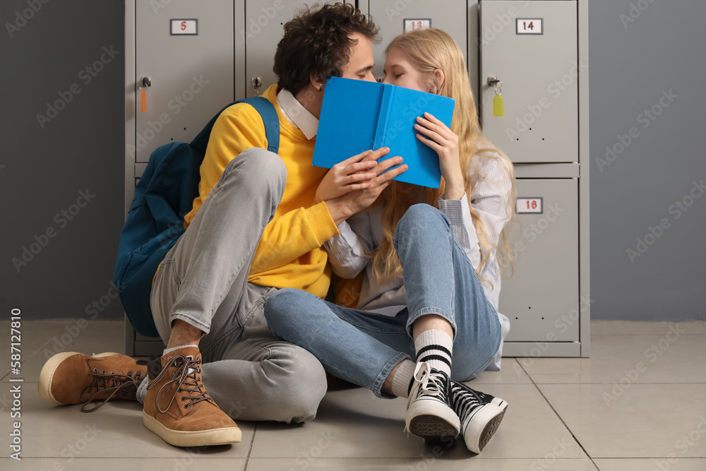 Cute teenage couple covering themselves with book near locker at school