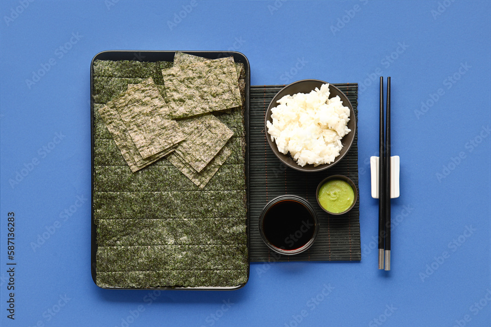 Plate with nori sheets, rice, wasabi and soy sauce on blue background