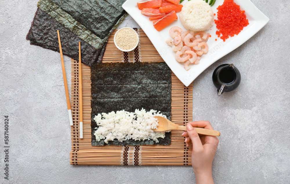 Woman preparing sushi rolls on light background