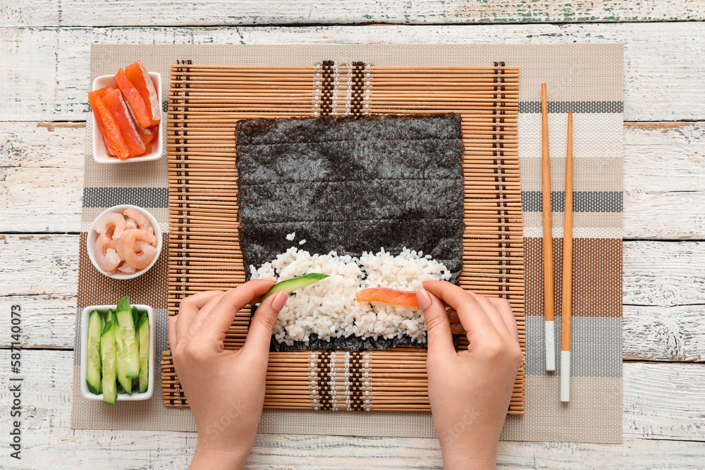 Woman preparing sushi rolls on light wooden background
