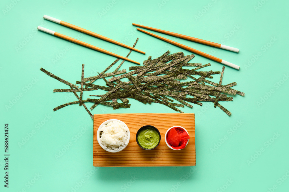 Wooden board with bowls of rice, ginger, wasabi and cut nori sheets on color background
