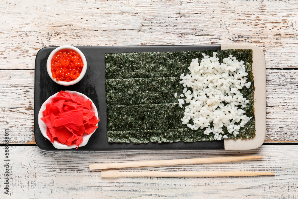 Board with nori and ingredients for preparing sushi rolls on light wooden background