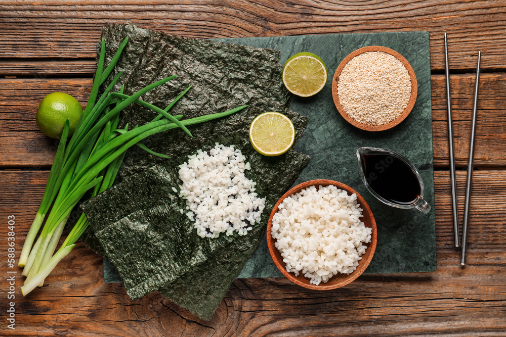 Slate board of nori with rice, sesame seeds and sauce on wooden background