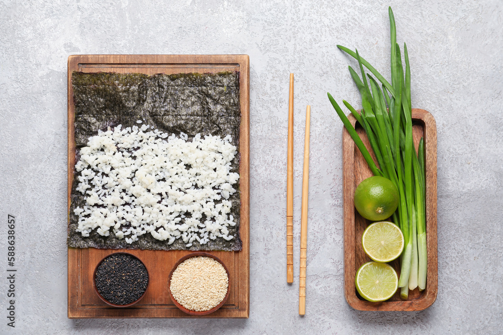 Wooden board with nori and ingredients for preparing sushi rolls on light background