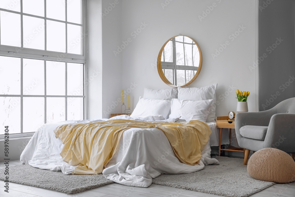 Interior of light bedroom with mirror and tulips in vase