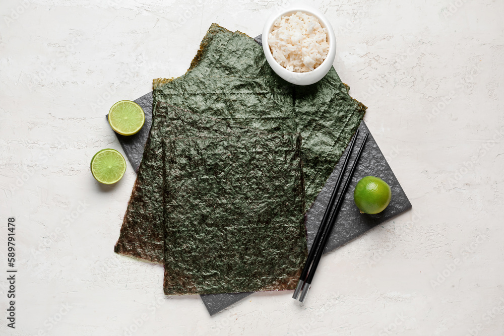 Slate board with nori sheets and rice on light background