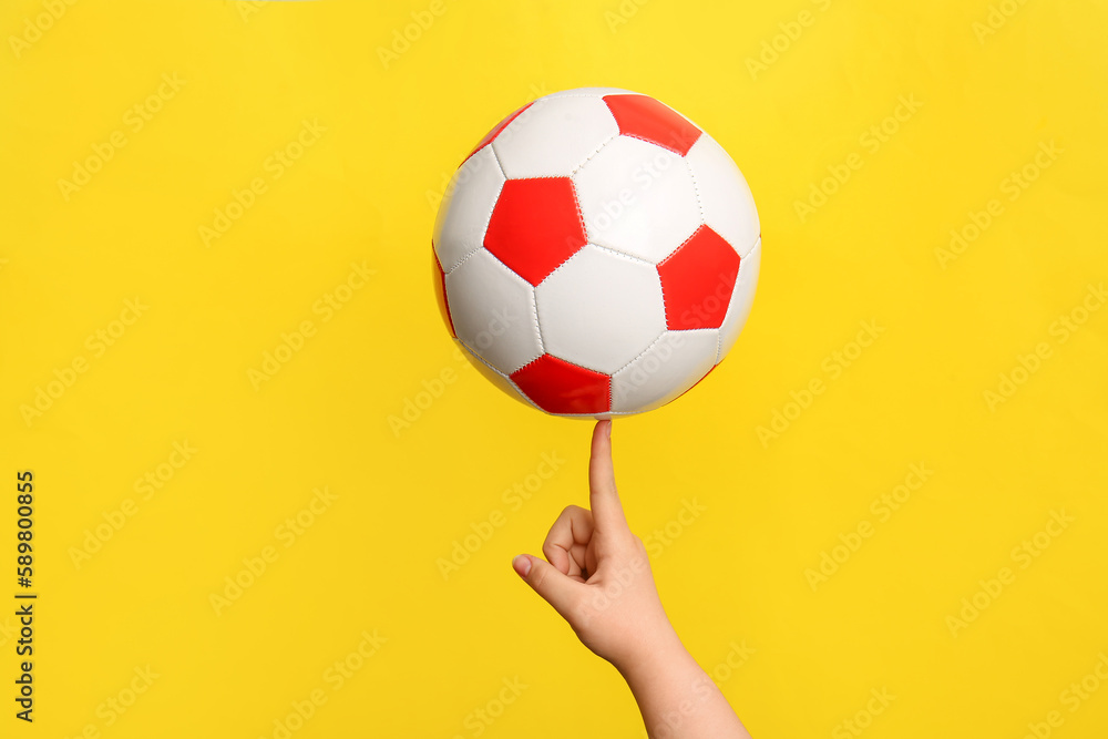 Childs hand with soccer ball on yellow background