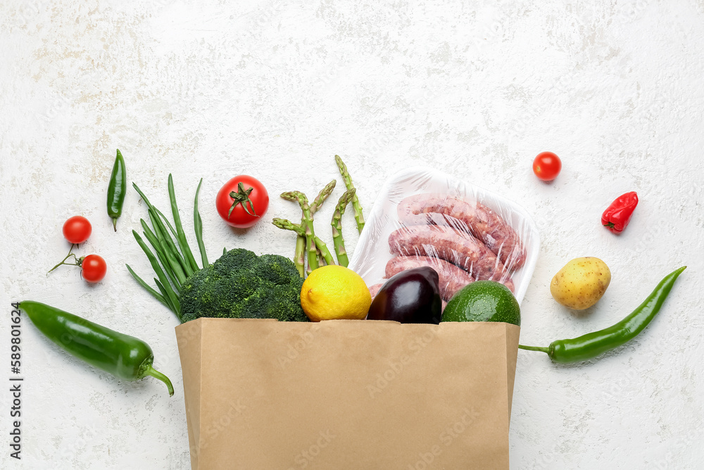 Paper bag with scattered vegetables and sausages on white background
