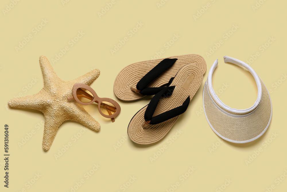 Flip-flops with sunglasses, starfish and cap on beige background