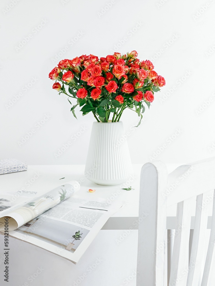 Vertical shot of a beautiful bouquet of roses in a white vase on a table with a magazine