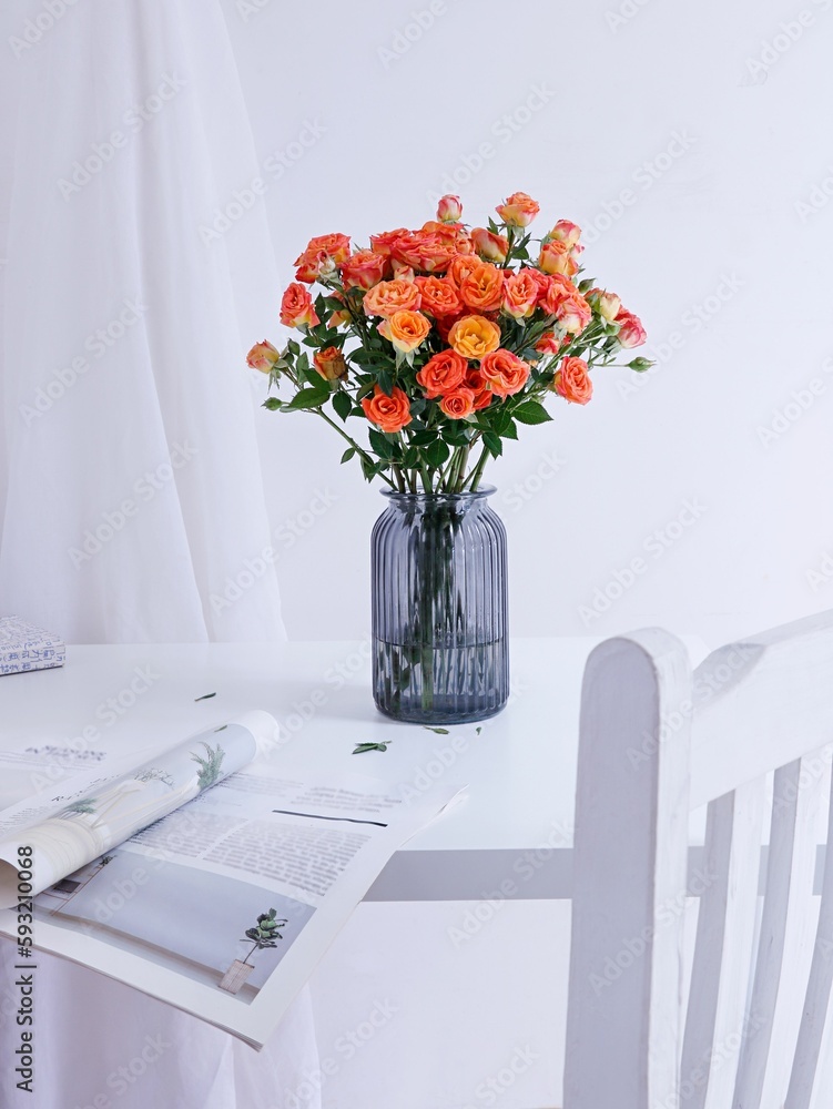 Vertical shot of a beautiful bouquet of roses in a blue glass vase on a white table with a magazine
