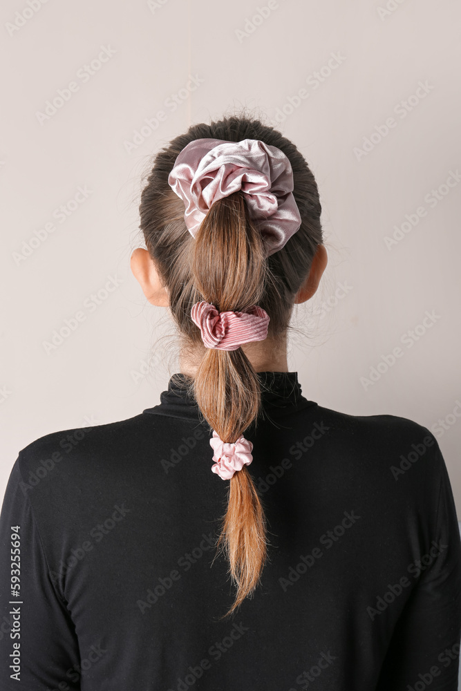 Woman with stylish hairdo and silk scrunchies on light background, back view