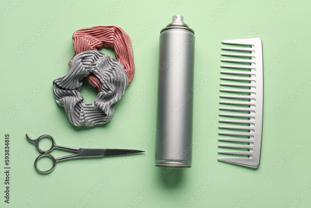 Bottle of hair spray, comb, scrunchies and scissors on color background