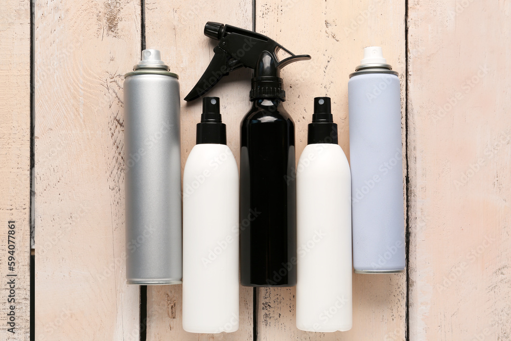 Different bottles of hair sprays on light wooden background