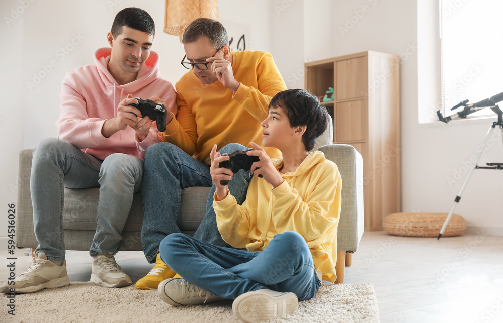 Happy little boy with his dad and grandfather playing video game at home