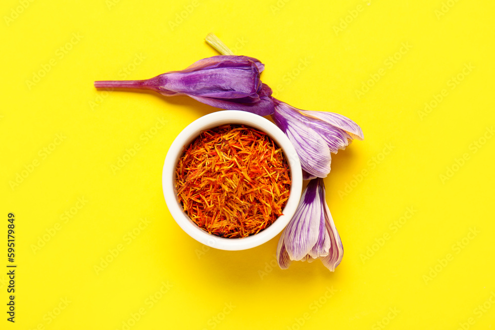 Bowl of dried saffron threads and crocus flowers on beige background