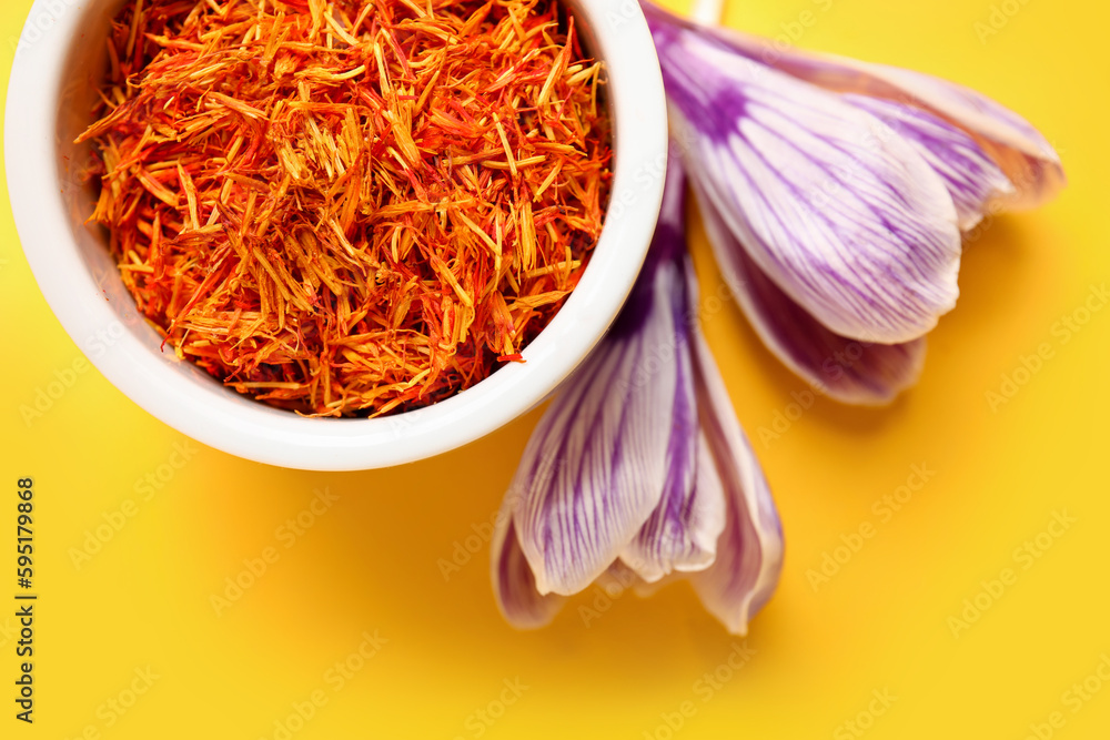 Bowl of dried saffron threads and crocus flowers on beige background