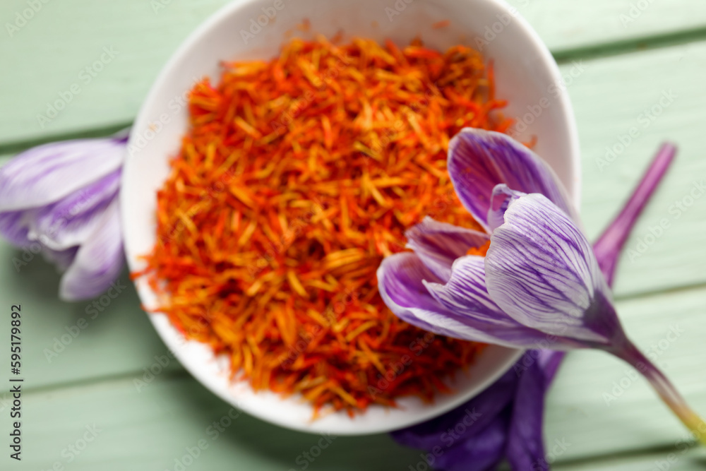 Bowl of dried saffron threads and crocus flowers on green wooden table