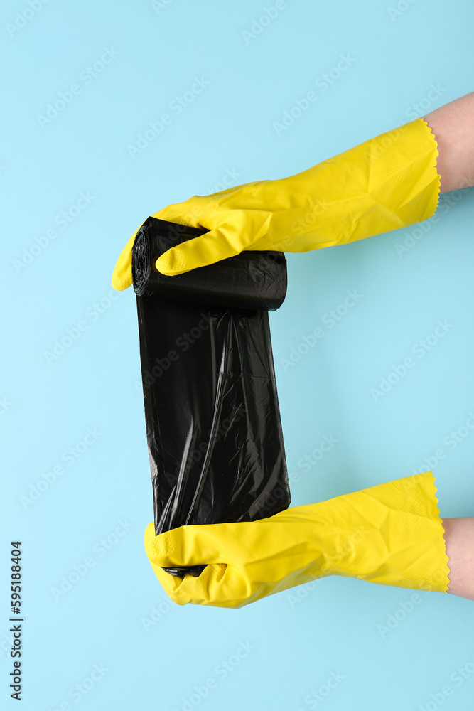 Hands in rubber gloves with garbage bags on blue background