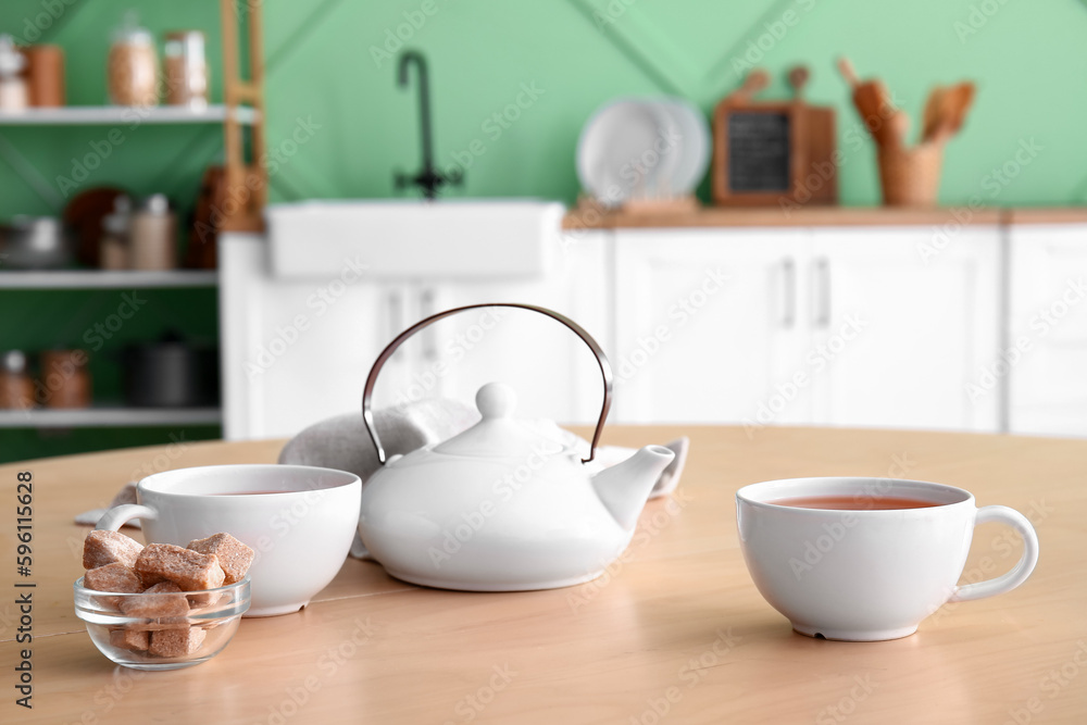 Teapot and cups on wooden table in kitchen