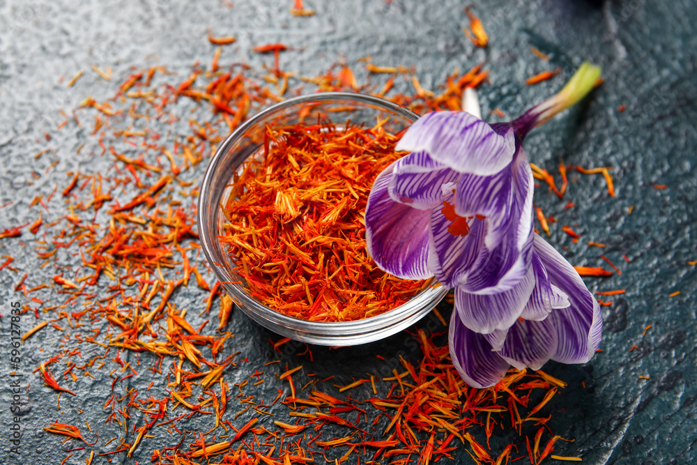 Bowl of dried saffron threads and crocus flowers on black table