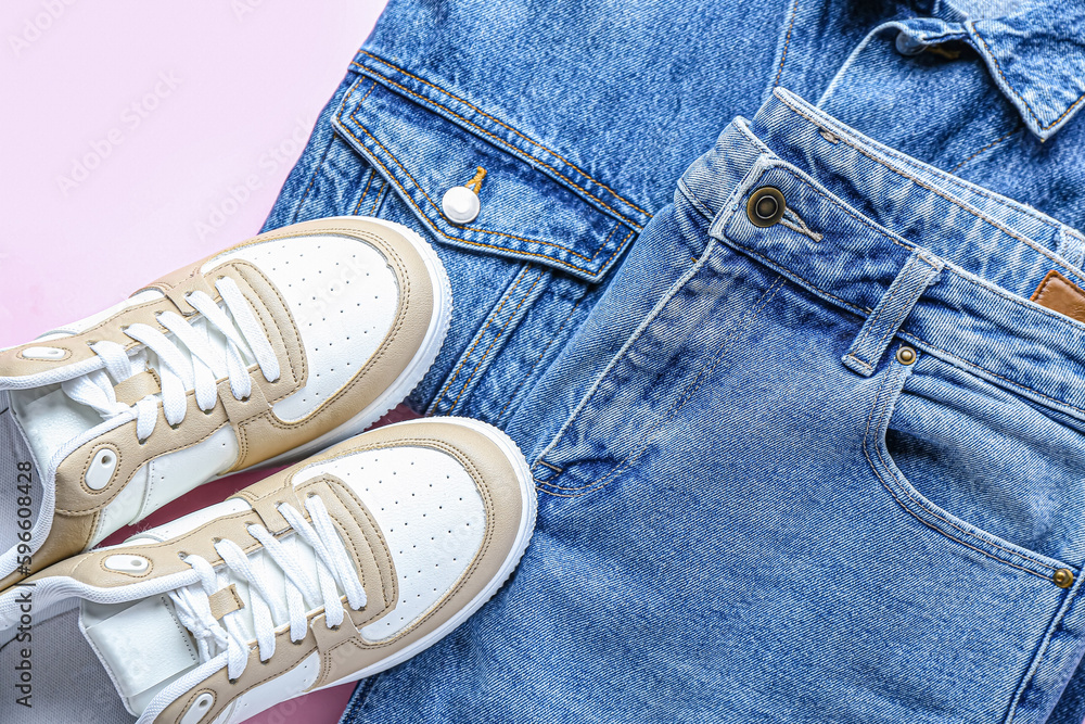 Stylish jeans with denim jacket and sneakers on pink background, closeup