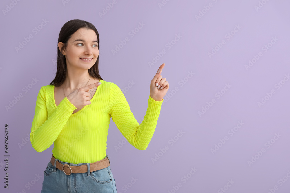 Young woman in bright shirt pointing at something on lilac background