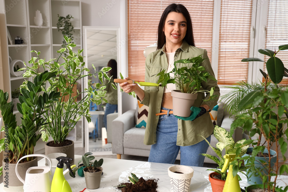 Young woman with shovel and green houseplants at home