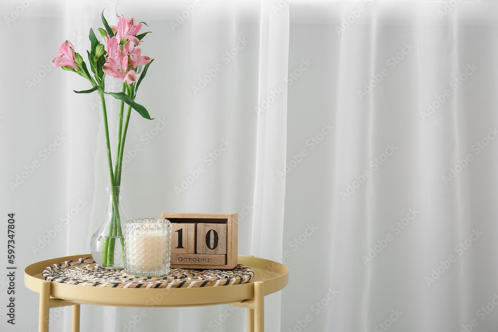 Vase with beautiful alstroemeria flowers, burning candle in holder and cube calendar with date 10th 
