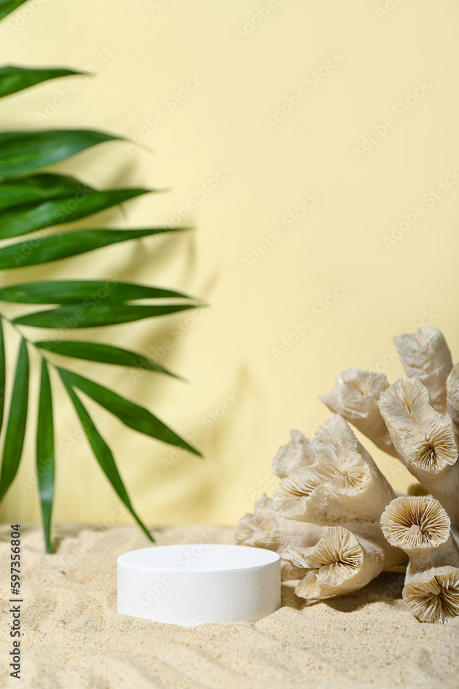 Decorative plaster podium, coral and palm leaves in sand on light background