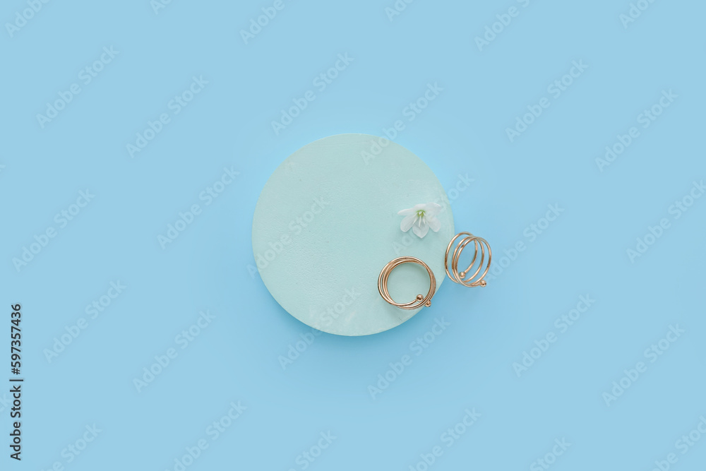 Showcase pedestal with golden rings and flower on blue background
