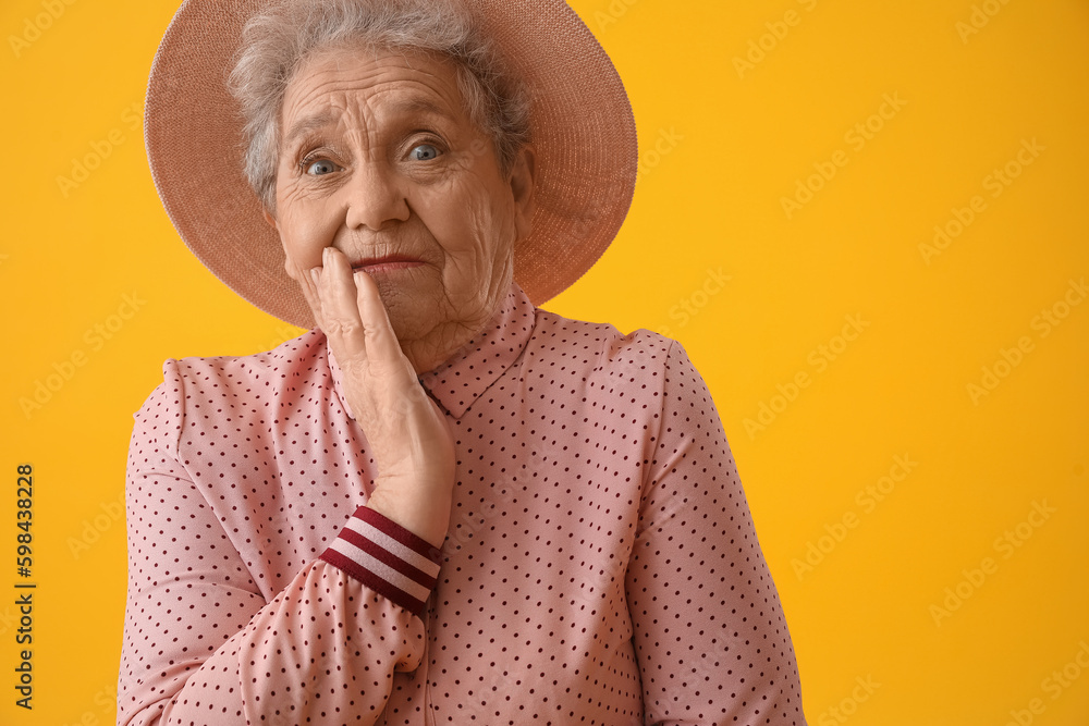 Shocked senior woman on yellow background, closeup