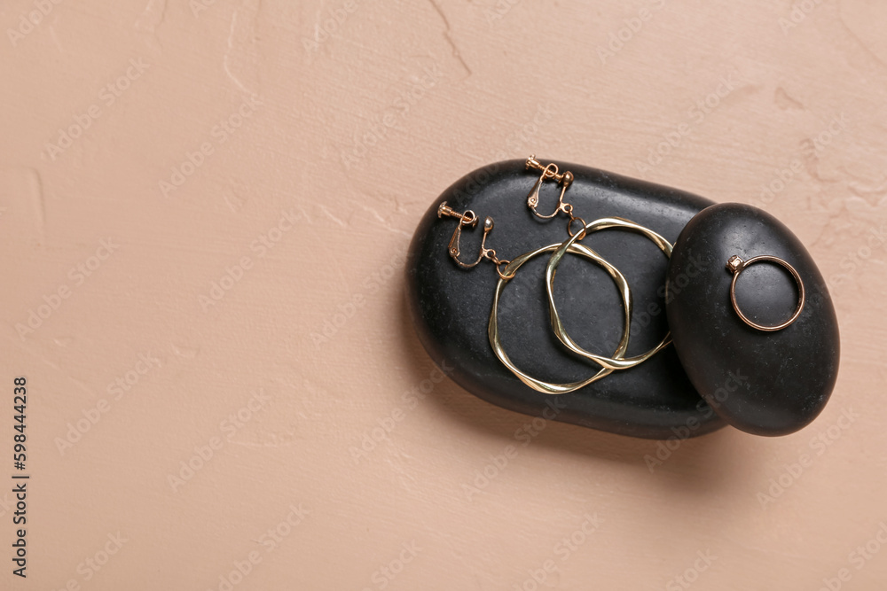 Black stones with golden earrings and ring on beige background