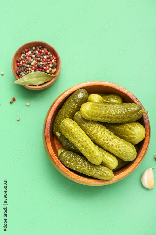 Bowl of tasty canned cucumbers with ingredients on pale green background