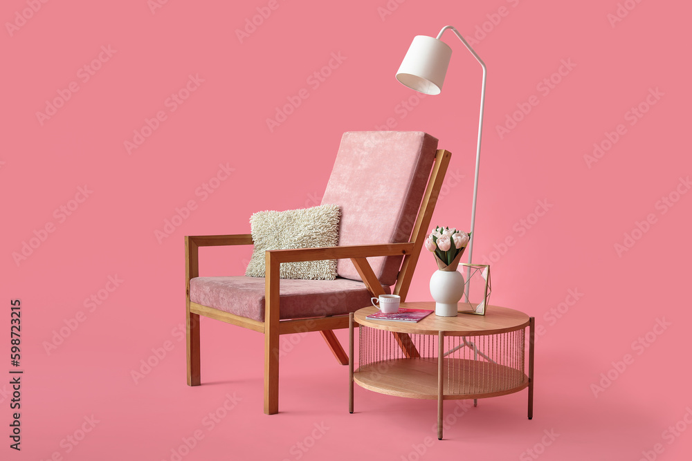 Coffee table with flower vase, magazine and cup of tea near cozy armchair on pink background