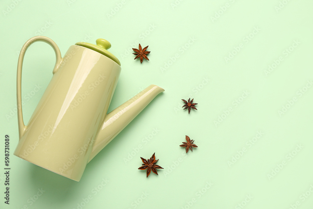 Ceramic teapot with spices on green background