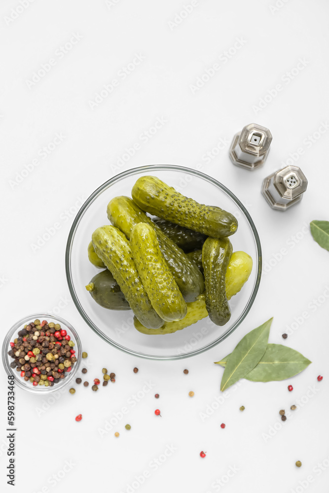 Bowl of tasty canned cucumbers with spices on white background