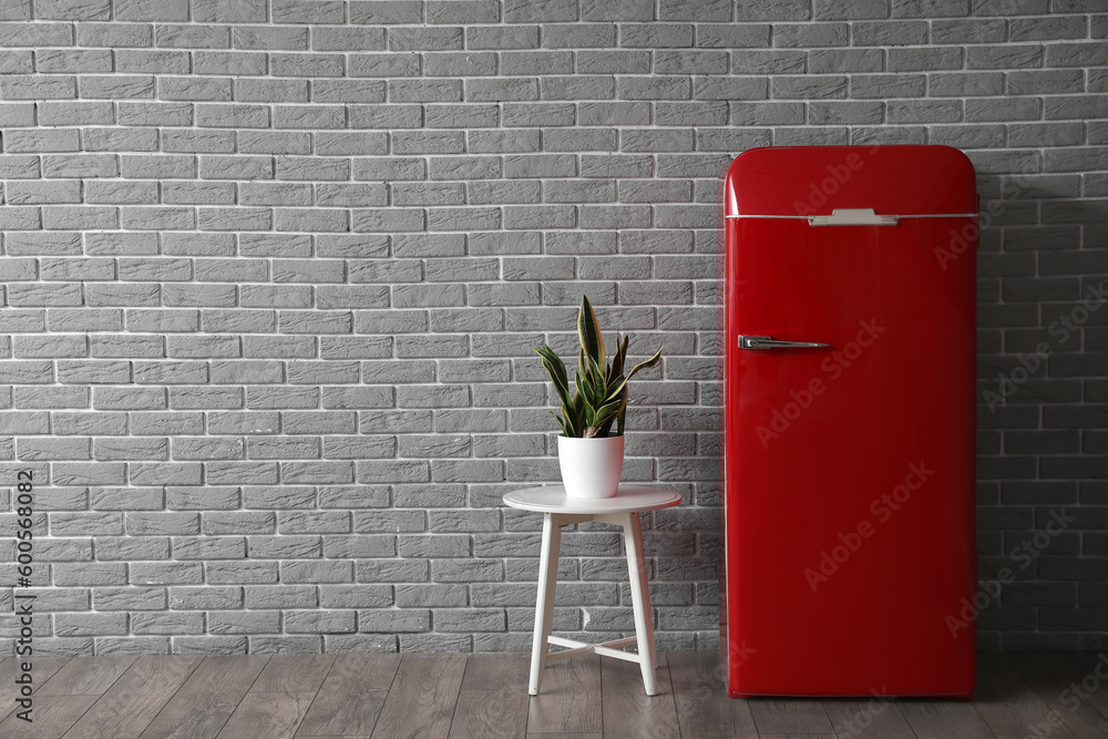 Stylish refrigerator and houseplant near brick wall in kitchen