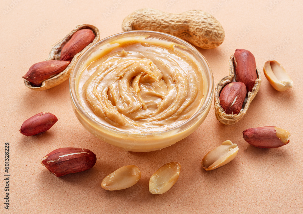 Bowl of peanut butter and peanuts around it on beige background.