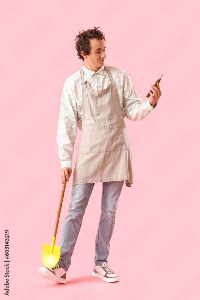 Male gardener with secateurs and shovel on pink background