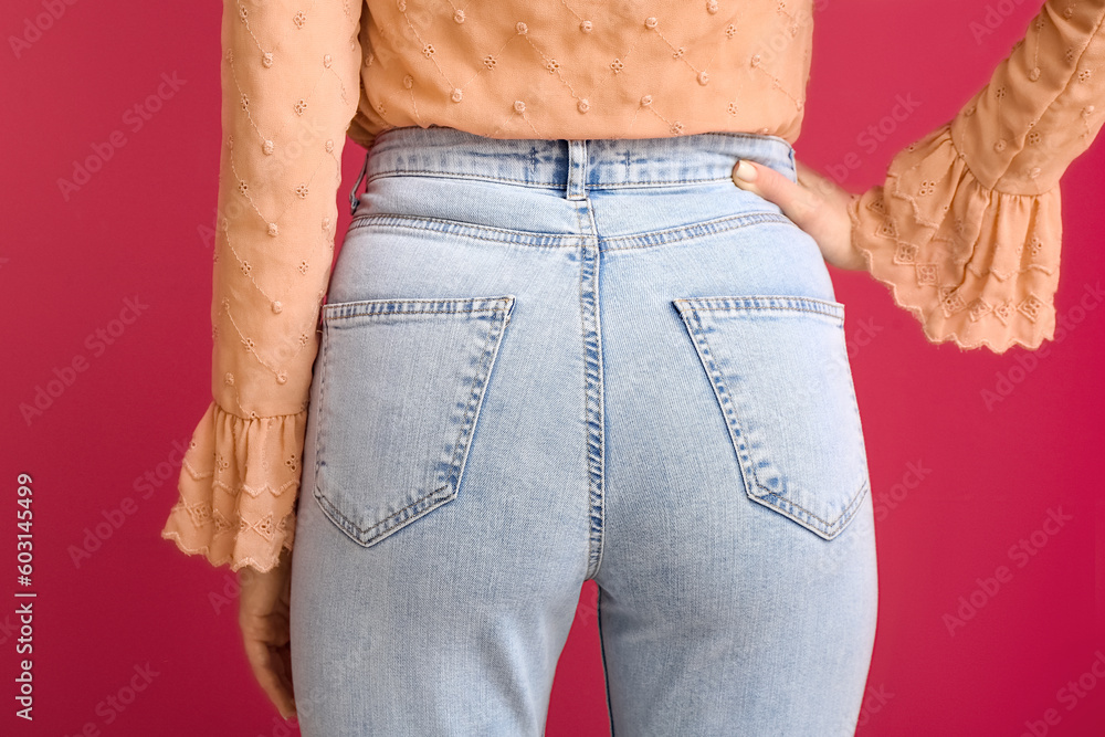 Young woman in stylish jeans on red background, back view