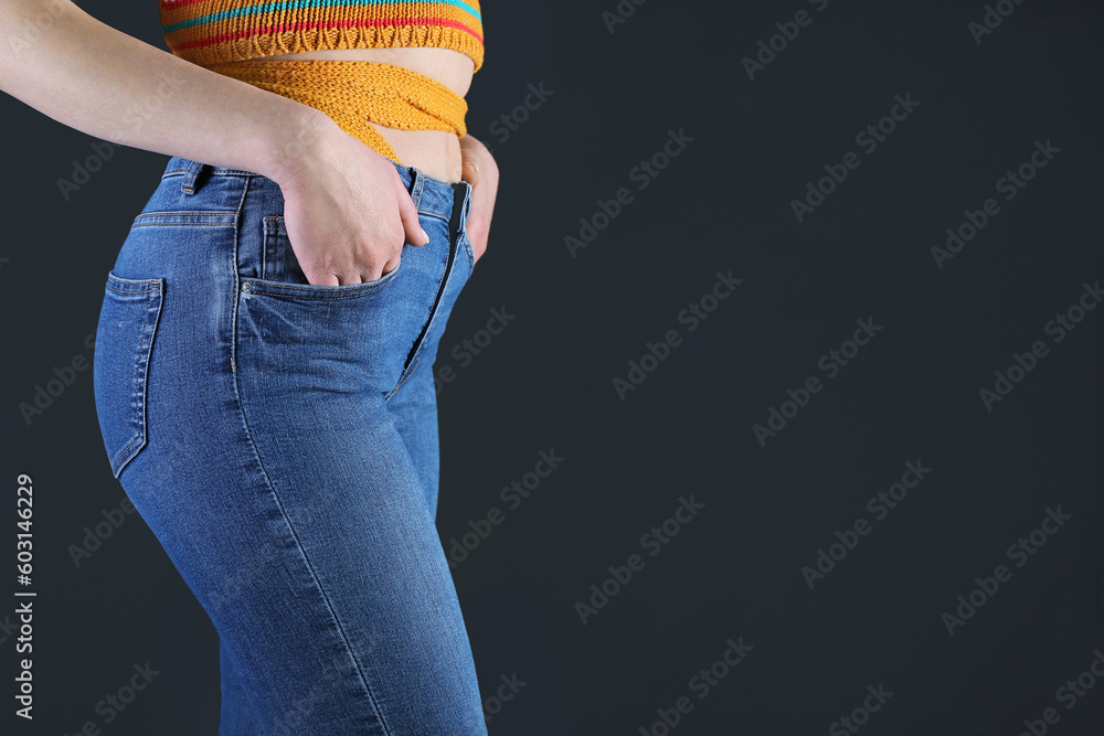 Young woman in skinny jeans on dark background, closeup