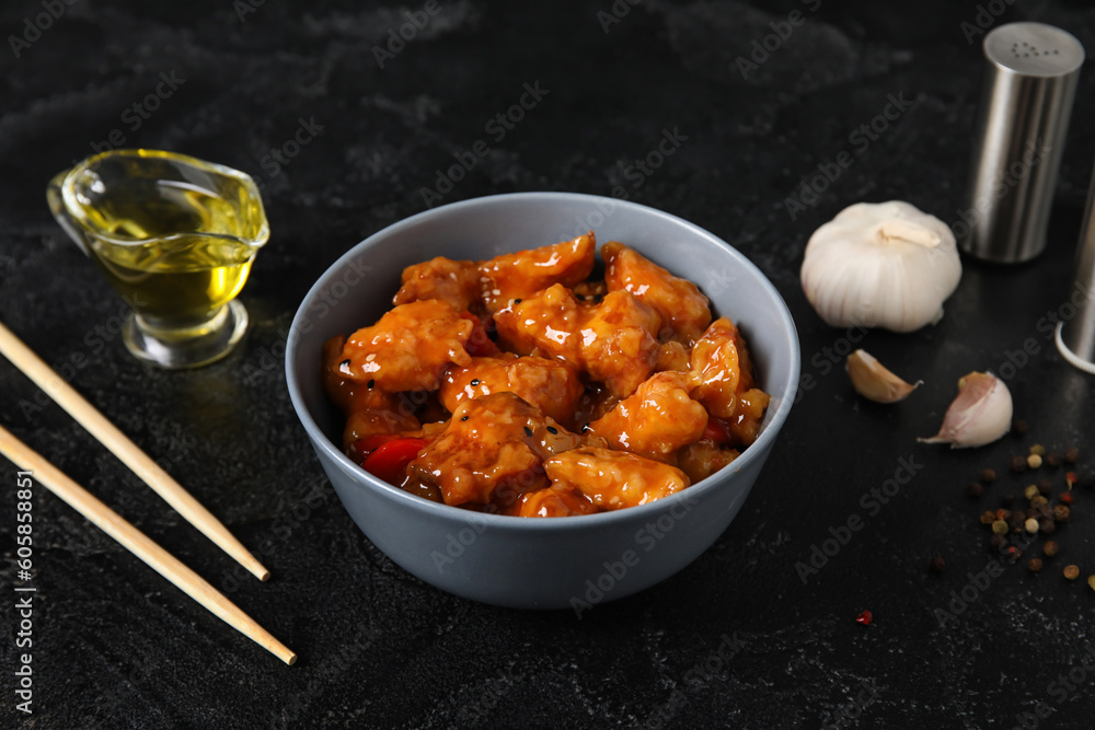 Tasty sweet and sour chicken in bowl with spices on dark background