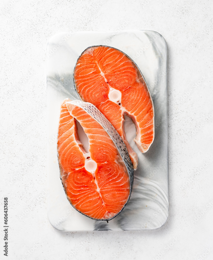 Fresh raw salmon steaks on marble board. Top view of fish on white background.