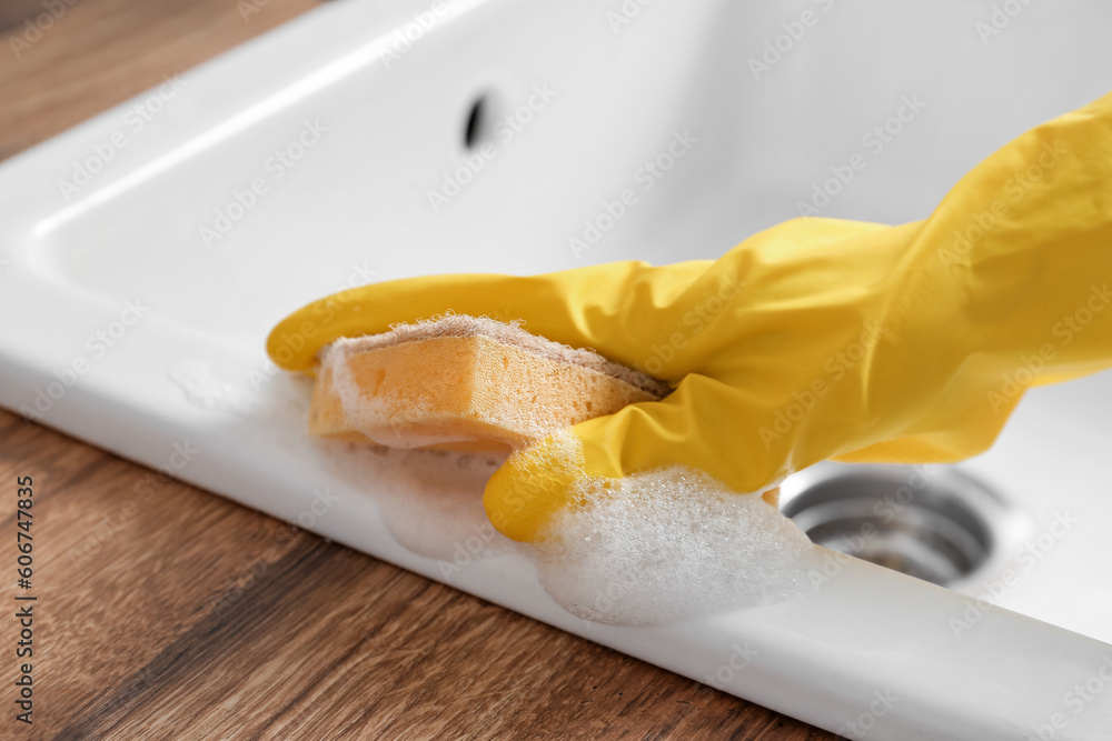 Woman cleaning sink with sponge in kitchen, closeup