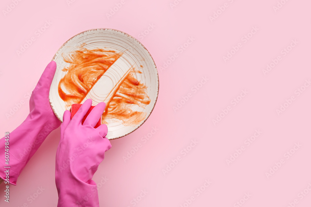 Female hands in rubber gloves washing dirty plate with sponge on pink background