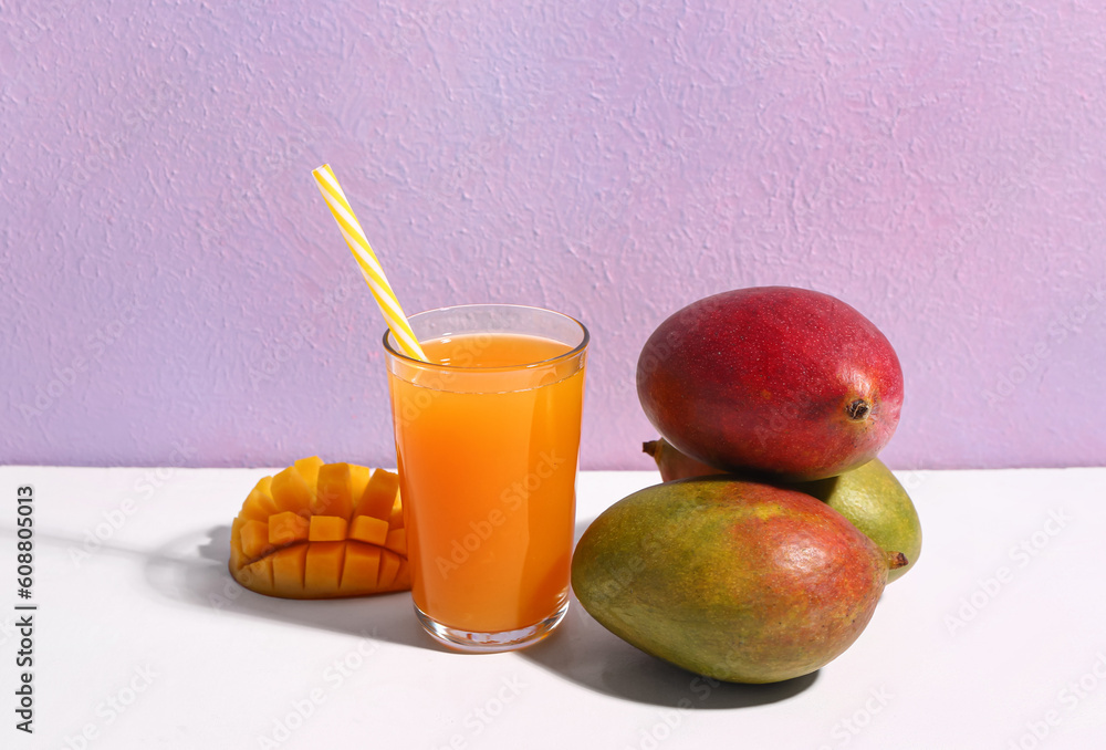 Glass of fresh mango smoothie on purple background